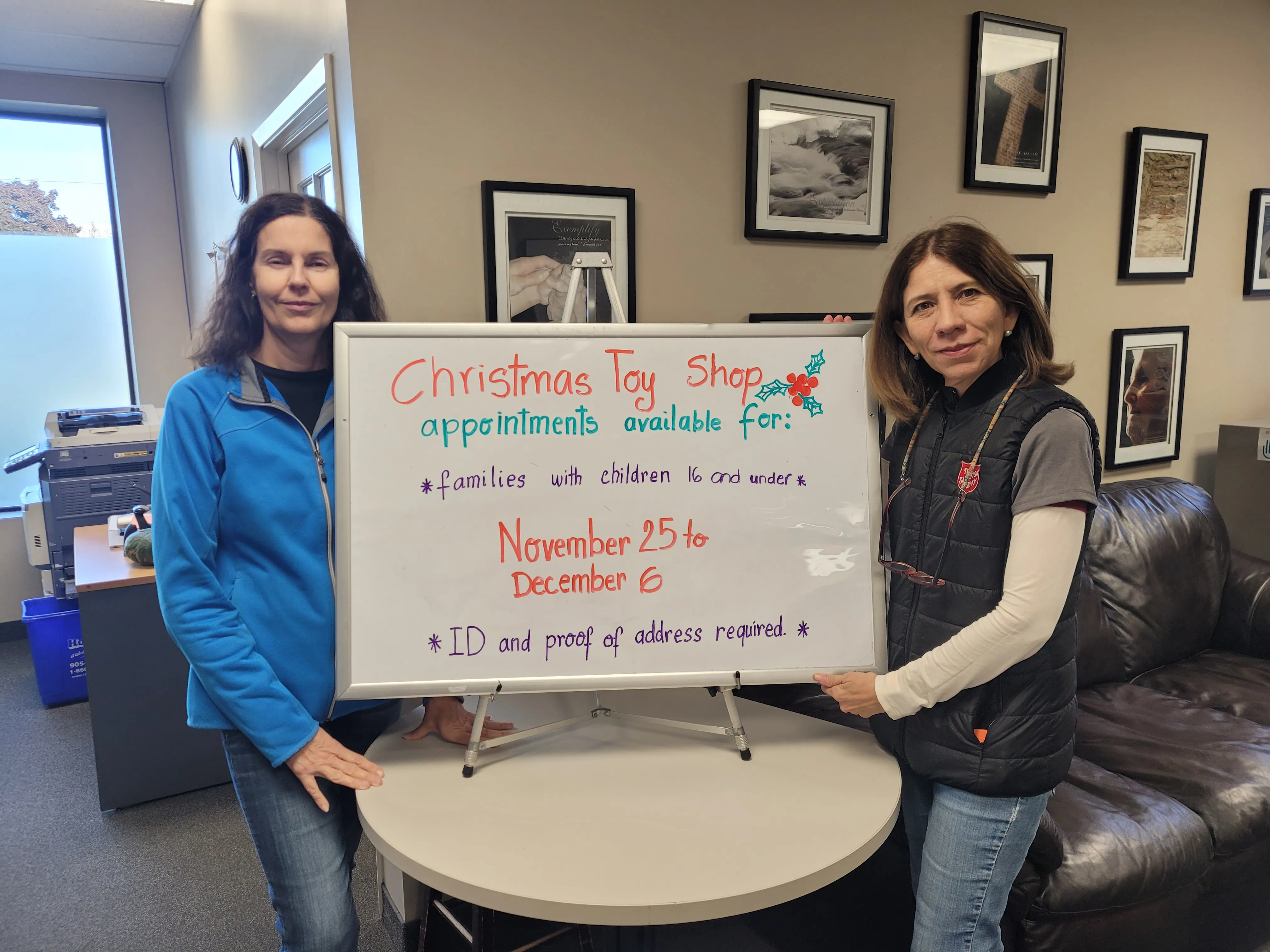 Two Khi Family Services staff stand in the office near a sign advertising appointment schedules